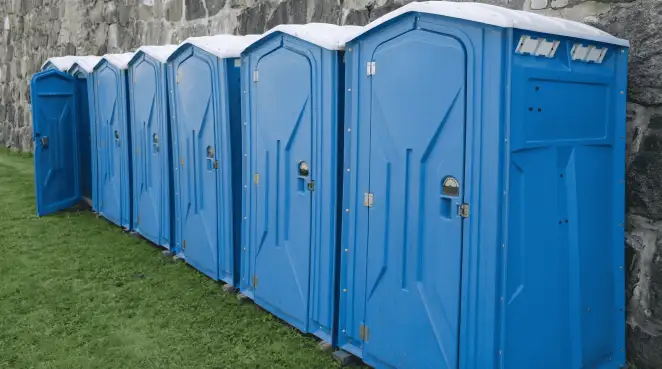 Row of blue portable toilets lined up on grass against a stone wall for event sanitation in Overland Park, KS