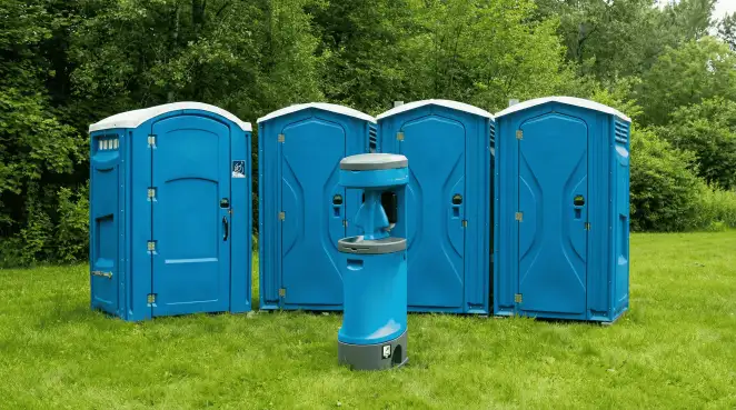 Four blue portable toilets and a matching hand washing station on grass near trees, a common sight at local outdoor events in Overland Park, KS