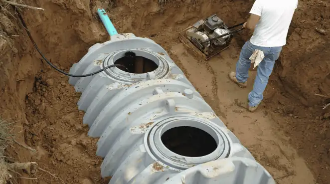 Septic tank installation showing a technician compacting soil around a new poly septic tank in an excavation pit in Overland Park, KS